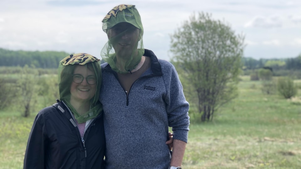 Laurie and Alexander are in the middle of a field with a fly net on their heads.